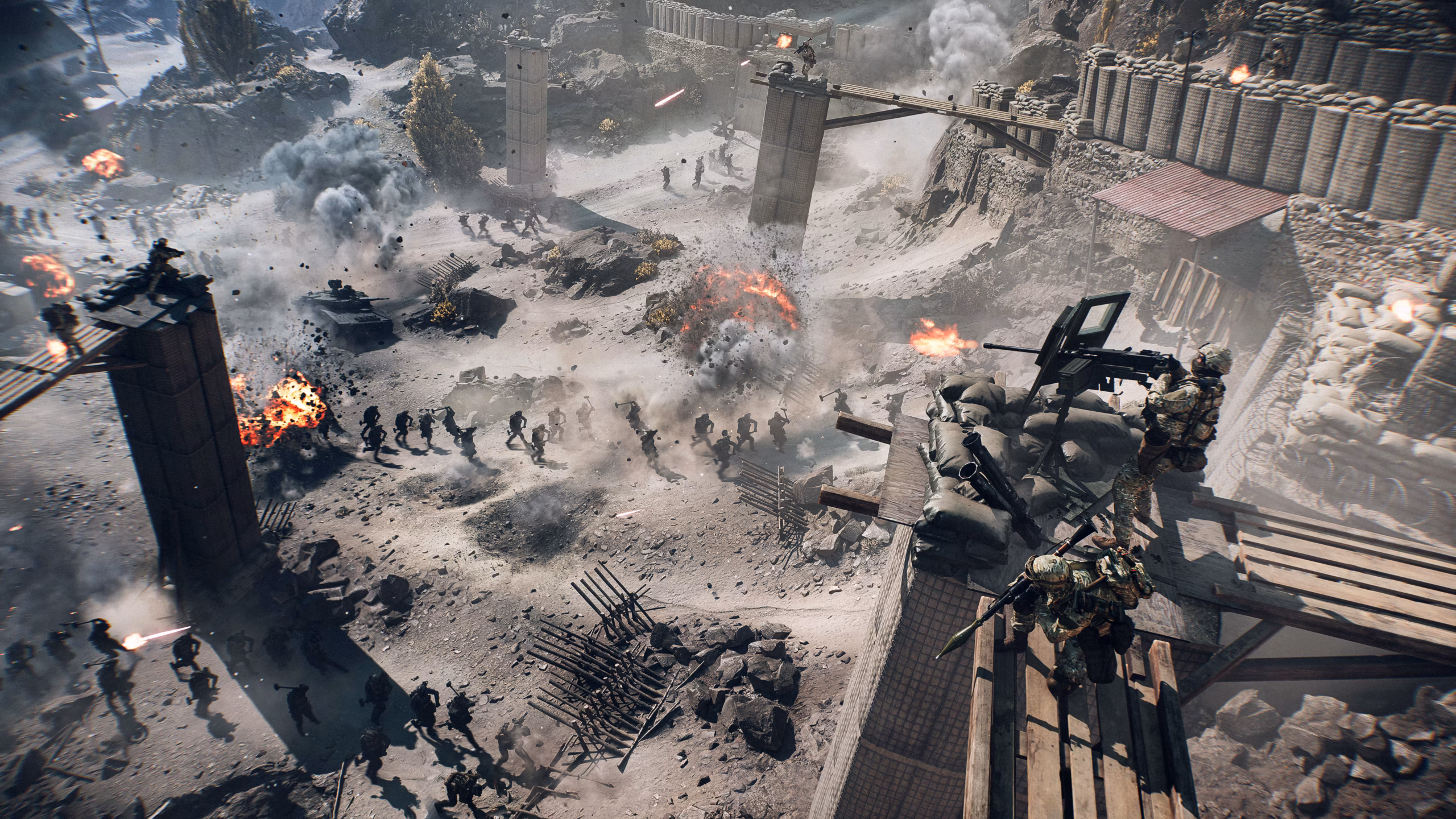 An in-game screenshot of a chaotic battlefield with several foot soldiers, military vehicles and machine gun turrets overlooking the scene.